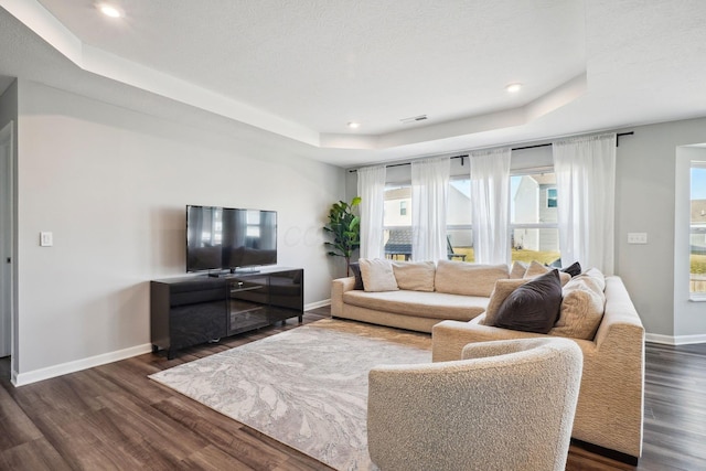 living area with visible vents, a raised ceiling, dark wood-type flooring, recessed lighting, and baseboards