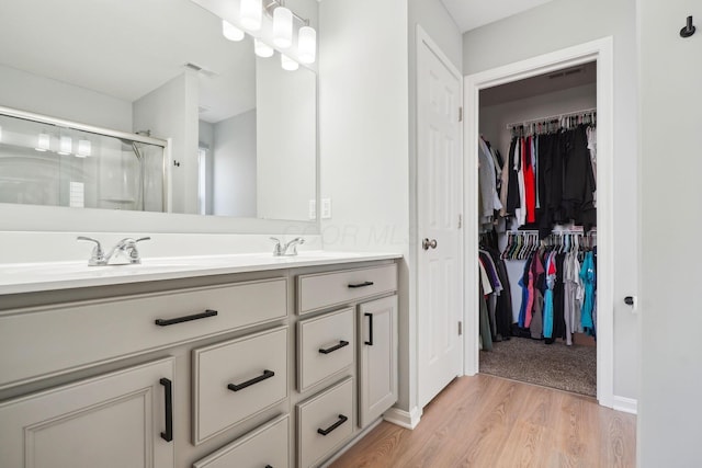 bathroom featuring visible vents, a shower stall, double vanity, wood finished floors, and a sink