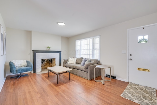 living room with light wood-type flooring, visible vents, baseboards, and a brick fireplace