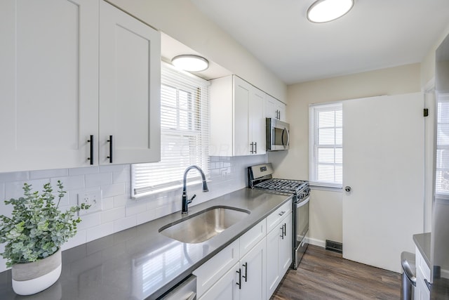 kitchen with a sink, decorative backsplash, dark wood-type flooring, white cabinets, and stainless steel appliances