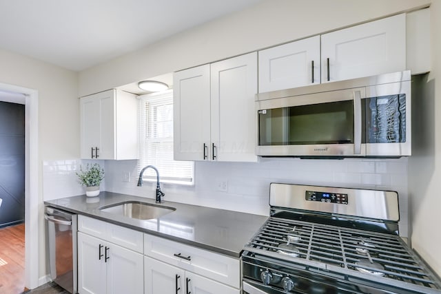 kitchen featuring a sink, stainless steel appliances, dark countertops, and white cabinetry