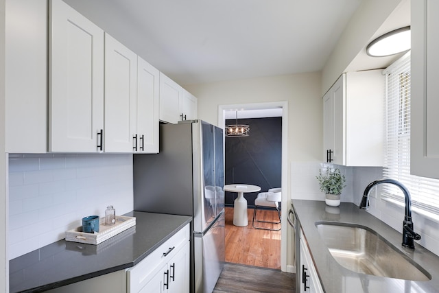 kitchen with dark countertops, tasteful backsplash, dark wood-style floors, white cabinets, and a sink