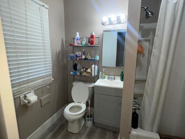 full bathroom featuring curtained shower, baseboards, toilet, wood finished floors, and vanity