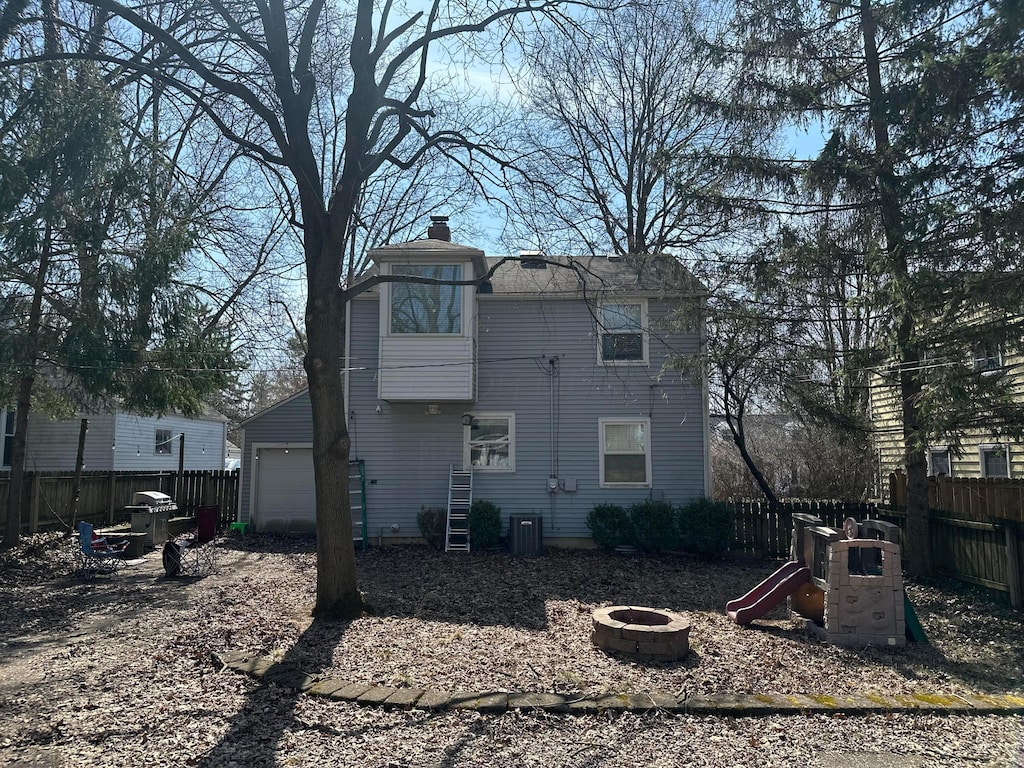 back of property featuring a playground, an outdoor fire pit, fence, a garage, and a chimney