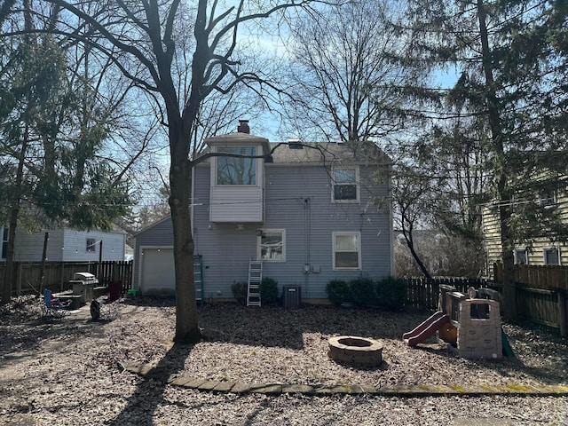 back of property featuring a playground, an outdoor fire pit, fence, a garage, and a chimney