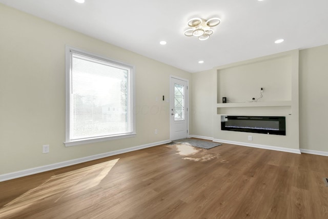 unfurnished living room with baseboards, built in shelves, and a glass covered fireplace