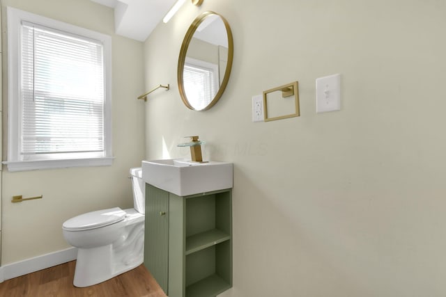 half bathroom with toilet, vanity, baseboards, and wood finished floors