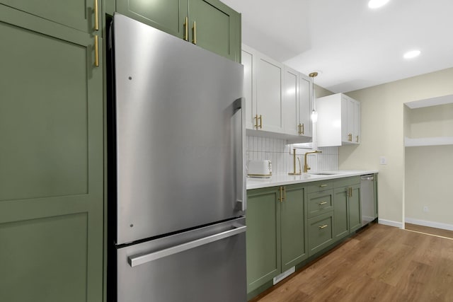 kitchen featuring a sink, stainless steel appliances, green cabinets, light countertops, and decorative backsplash