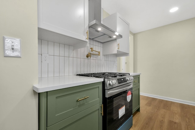 kitchen featuring tasteful backsplash, gas range, light countertops, wall chimney exhaust hood, and green cabinetry