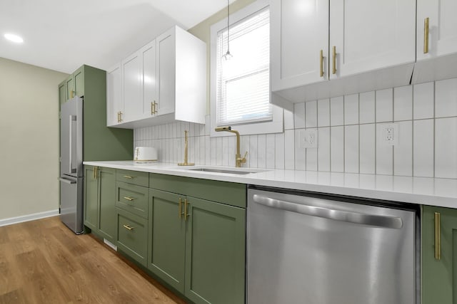 kitchen featuring a sink, stainless steel appliances, light countertops, green cabinets, and tasteful backsplash