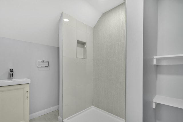 full bathroom with tiled shower, vanity, baseboards, and vaulted ceiling