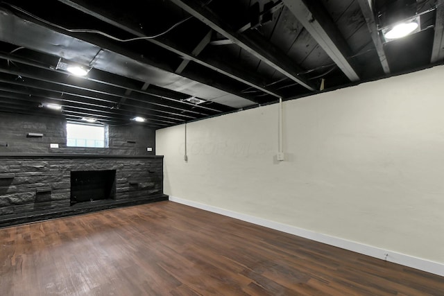 below grade area with a stone fireplace, baseboards, and wood finished floors