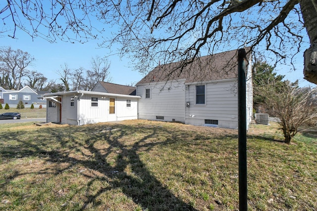 back of property with cooling unit, a lawn, roof with shingles, and crawl space