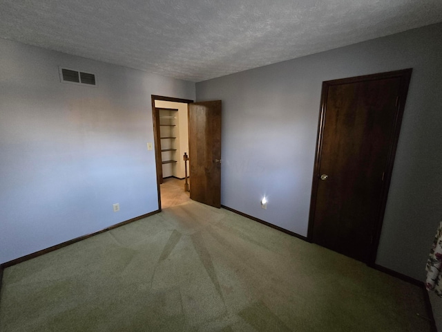 unfurnished bedroom featuring light carpet, visible vents, a textured ceiling, and baseboards