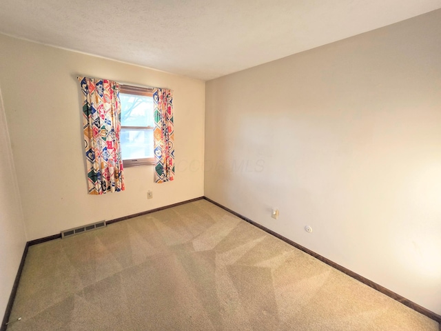 carpeted spare room with visible vents, baseboards, and a textured ceiling