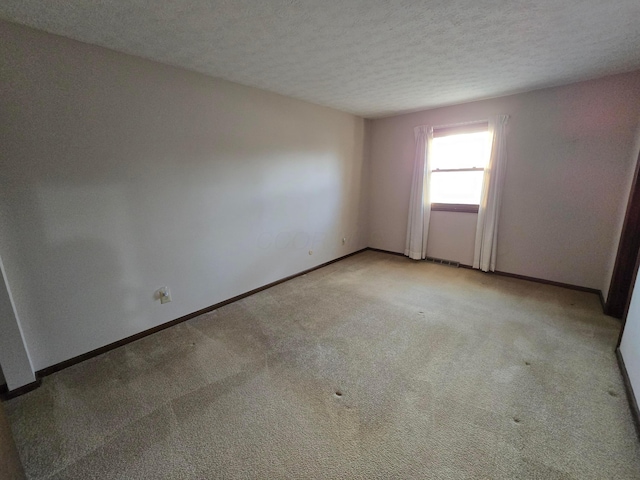 unfurnished room featuring visible vents, light colored carpet, a textured ceiling, and baseboards