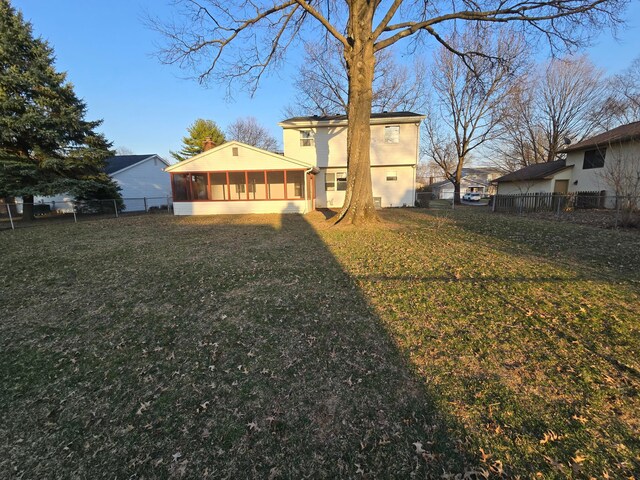 back of house featuring stucco siding, a lawn, fence, and a sunroom