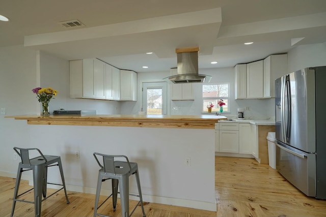 kitchen featuring visible vents, white cabinets, a kitchen breakfast bar, island range hood, and stainless steel fridge