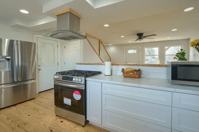 kitchen featuring a ceiling fan, stainless steel appliances, island range hood, light wood finished floors, and light stone countertops