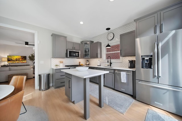 kitchen with gray cabinets, a sink, stainless steel appliances, glass insert cabinets, and light wood-type flooring