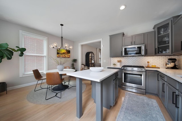 kitchen featuring backsplash, stainless steel appliances, light countertops, and an inviting chandelier