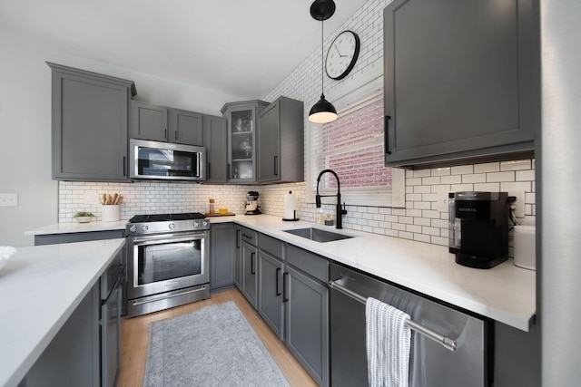 kitchen featuring pendant lighting, light wood-type flooring, light countertops, appliances with stainless steel finishes, and a sink