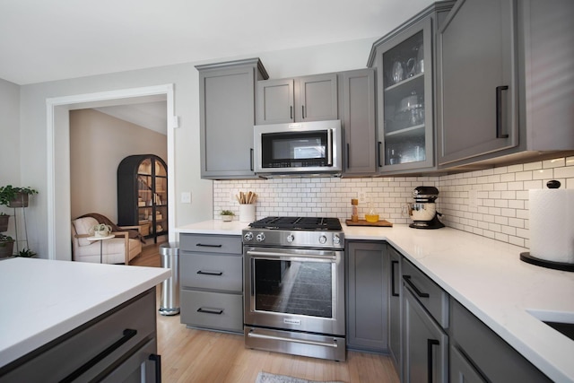 kitchen featuring light wood finished floors, gray cabinetry, light countertops, appliances with stainless steel finishes, and backsplash