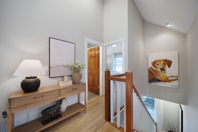 corridor featuring lofted ceiling, light wood-style flooring, and an upstairs landing