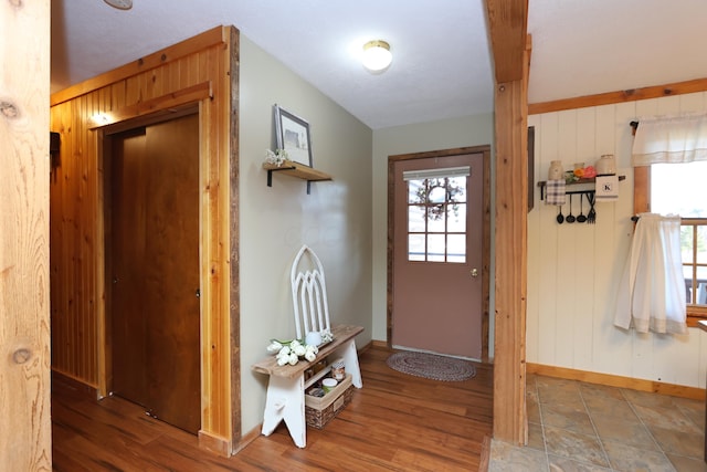 doorway to outside with baseboards, wooden walls, a healthy amount of sunlight, and wood finished floors