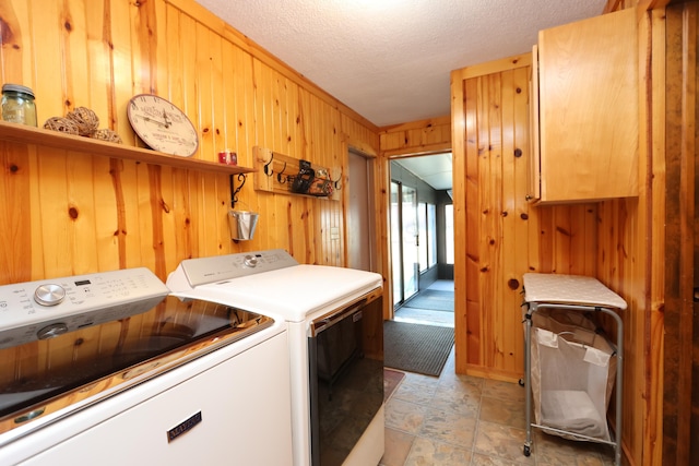 clothes washing area featuring cabinet space, wooden walls, washing machine and dryer, and a textured ceiling