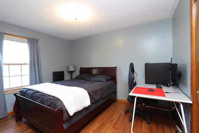 bedroom with baseboards, wood finished floors, visible vents, and a textured ceiling