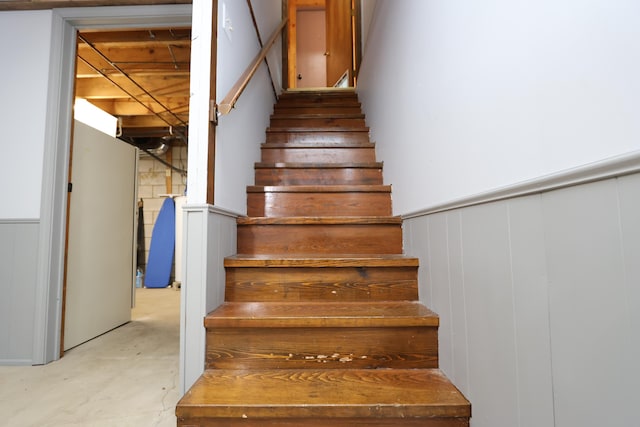 stairs featuring wainscoting and unfinished concrete flooring