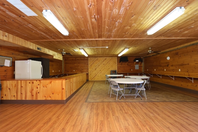 kitchen with wood walls, wooden ceiling, freestanding refrigerator, wood finished floors, and a ceiling fan