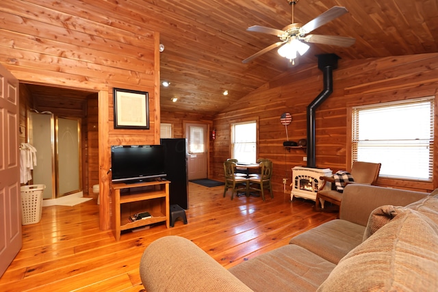 living area with wooden walls, wood ceiling, light wood-style flooring, and a wood stove