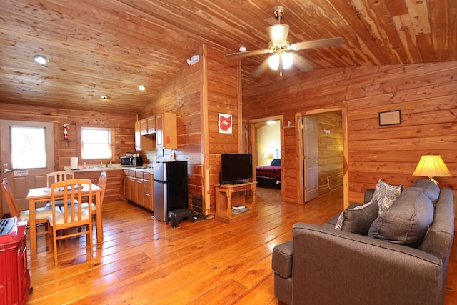 living area with wood walls, light wood-type flooring, vaulted ceiling, wooden ceiling, and a ceiling fan