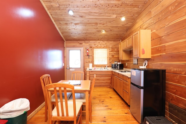 kitchen with wood walls, light wood-style flooring, wooden ceiling, stainless steel appliances, and a sink