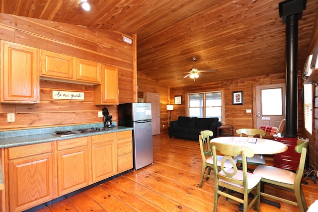 kitchen with light brown cabinets, wood walls, a wood stove, stainless steel appliances, and a ceiling fan