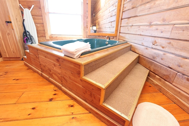 bathroom featuring wood-type flooring, a garden tub, and wood walls