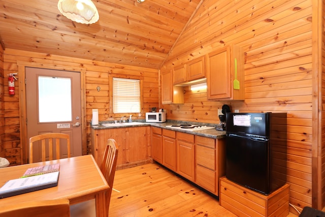 kitchen with white appliances, light wood finished floors, lofted ceiling, a sink, and wood walls