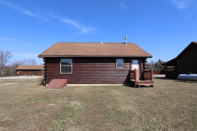 back of house featuring log exterior, a yard, and roof with shingles