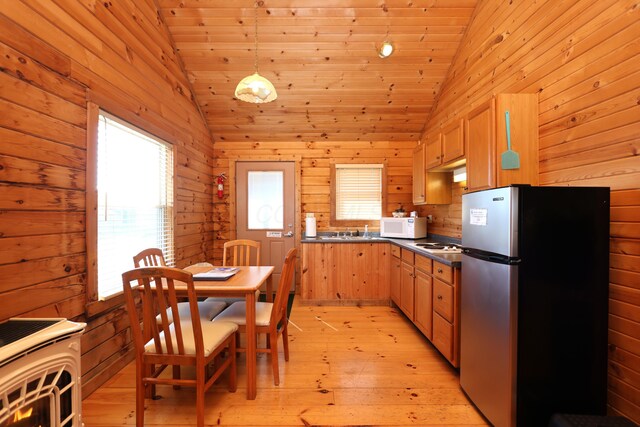 kitchen with dark countertops, white microwave, light wood finished floors, vaulted ceiling, and freestanding refrigerator