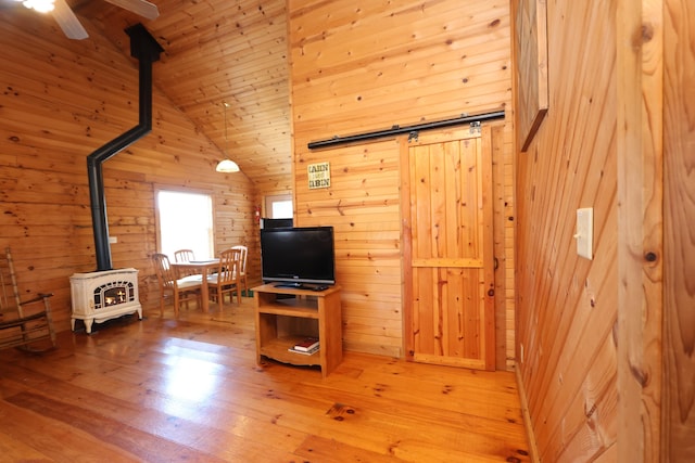 living area featuring high vaulted ceiling, wooden walls, light wood finished floors, wood ceiling, and a wood stove