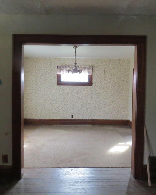 unfurnished dining area with wallpapered walls, baseboards, and wood-type flooring