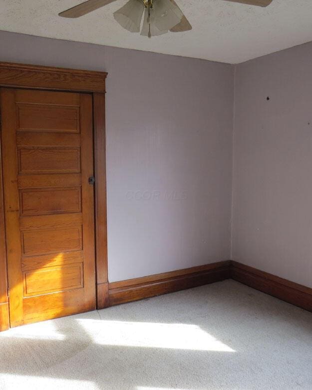 unfurnished room with a textured ceiling, carpet, baseboards, and ceiling fan