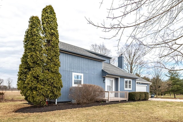 view of side of property featuring a yard, roof with shingles, a chimney, and an attached garage