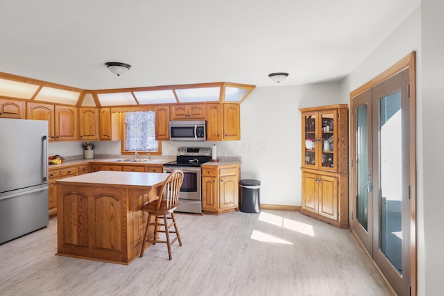 kitchen with a breakfast bar, a sink, appliances with stainless steel finishes, light wood-type flooring, and a center island