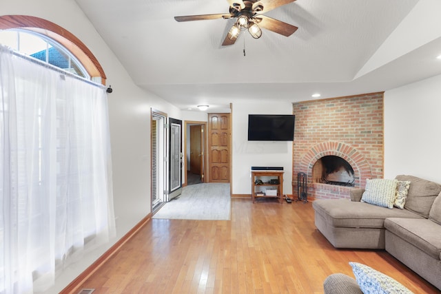 living room featuring light wood finished floors, baseboards, a brick fireplace, ceiling fan, and vaulted ceiling