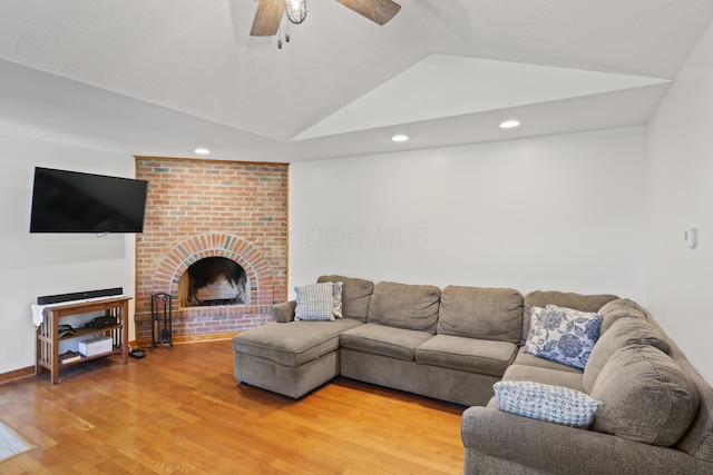 living area with recessed lighting, ceiling fan, vaulted ceiling, light wood-style floors, and a brick fireplace