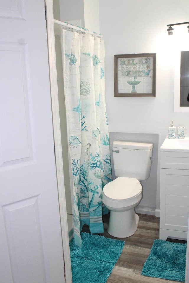 bathroom with curtained shower, toilet, wood finished floors, and vanity