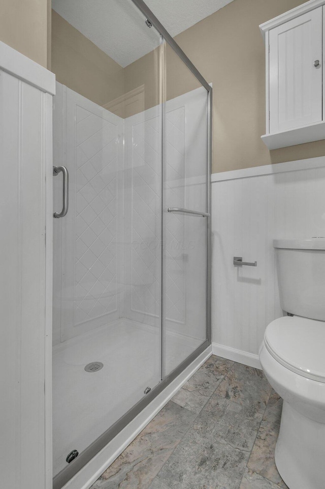 bathroom with a wainscoted wall, toilet, and a shower stall